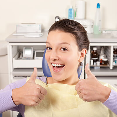 A girl sitting in the dentist's chair and smiling happily with her thumbs up